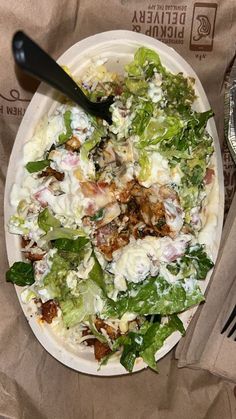 a white plate topped with salad next to a fork and paper bag on top of a table