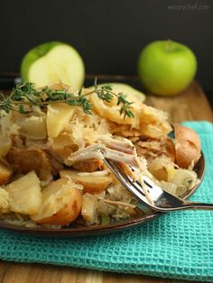 a plate with some food on it next to two apples and a fork in it