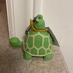 a green turtle keychain with a tag attached to it's back sitting on a counter