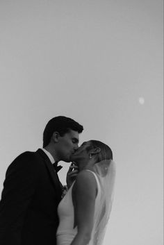 a bride and groom kissing each other in front of a white sky with the sun behind them