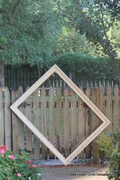 a wooden fence with a diamond shaped mirror on it's side in front of some flowers