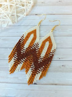 a pair of beaded earrings on top of a white wooden table next to a vase