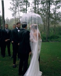 a bride and groom standing under an umbrella in the rain while other people look on