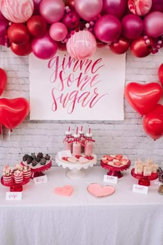 a table topped with lots of red and pink balloons next to a sign that says yummy sweet sugar