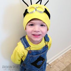 a little boy wearing a yellow shirt and overalls with a bee hat on his head