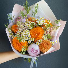 a bouquet of flowers is being held by someone's hand in front of a gray wall