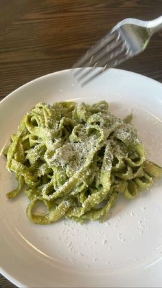 a white plate topped with pasta covered in pesto sauce and a fork next to it