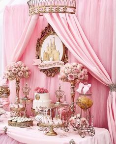 a table topped with lots of cakes and desserts next to a pink drapes