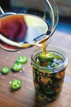 a jar filled with green peppers being poured into the jar to make pickled jalapenos