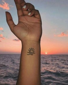 a person's arm with a small sun tattoo on it, and the ocean in the background