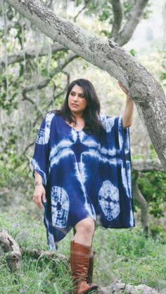 a woman wearing boots and a blue dress is standing in the grass under a tree