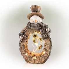 a snowman sitting on top of a tree stump holding a wreath with lights in it