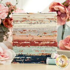 a stack of folded fabric sitting on top of a wooden table next to pink flowers