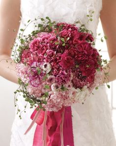 a woman holding a bouquet of flowers in her hand and wearing a white dress with pink ribbon