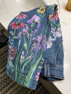 a blue jean jacket with flowers painted on it sitting in front of a white sink