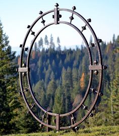 a circular sculpture in the middle of a grassy area with trees and mountains in the background