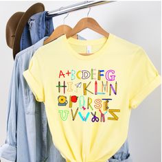 Alphabet Doodle Teacher Shirt, Alphabet Shirt, Teacher Appreciation T-Shirt, Kindergarten, First Grade, Second Grade, Cute Teacher Tee This unisex t-shirt fits like a well-loved favorite. It has a soft and light feel, with just the right amount of stretch. * Made of combed and ring-spun cotton * Comfortable and flattering for both men and women SIZING * See sizing chart illustration. * If unsure as to what size to order, lay a favorite t-shirt flat and measure from armpit to armpit (width) and t Daycare Shirts, Shirts For Teachers, Alphabet Shirt, Thankful Shirt, Teaching Shirts, Teacher Tees, Teacher Outfits, Mom Tees, Shirt Fits