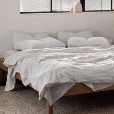 an unmade bed with white sheets and pillows on it in front of a window