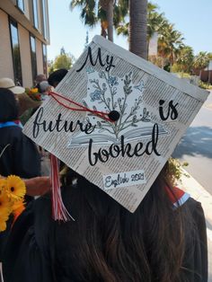 Graduation cap with a newspaper background and a book with flowers coming out of it in the center. It says “my future is booked” and at the bottom it says “English 2021” Decorated College Graduation Caps, Book Lover Graduation Cap, High School Cap Ideas, Cute Graduation Caps High Schools, English Major Graduation Party Ideas, English Major Cap Decoration, English Grad Caps