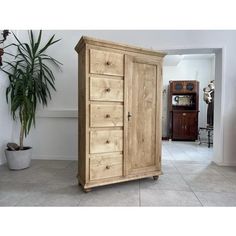 a tall wooden cabinet sitting next to a potted plant on top of a tile floor