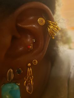 a woman's ear is adorned with gold and colorful earrings, including an earring