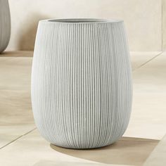 a large white vase sitting on top of a floor next to a planter in a room