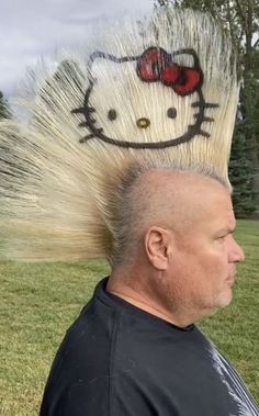 a man with a hello kitty haircut on top of his head in the grass