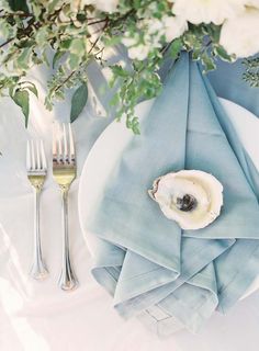 an oyster shell on a plate next to silverware and greenery with white flowers