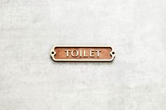 a wooden sign that says toilet on the side of a concrete wall with rivets