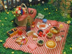 a picnic is set out on the grass with fruit and bread in baskets, wine bottles, and flowers