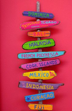 a wooden sign that has different languages on it in front of a pink wall with other signs