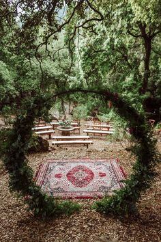 an outdoor area with benches, rug and trees in the background is surrounded by greenery