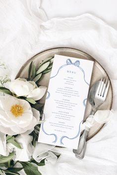 a table setting with white flowers, silverware and menu card on a metal platter