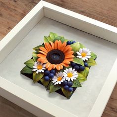 a white box with an orange flower and some blue berries in the center on a wooden table