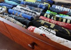 an open drawer filled with folded shirts on top of wooden drawers in a room next to a wall