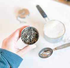 a person holding a cup filled with tea next to spoons