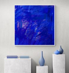 an abstract painting hangs on the wall next to two vases and a white table