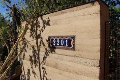 a house number plate on the side of a wall with trees in the background and bushes growing up against it