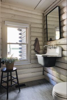 a white toilet sitting next to a bathroom sink under a window in a wooden cabin