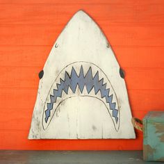 a wooden shark head on the side of a building with an orange wall behind it