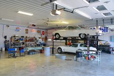 a white car is on top of a lift in a garage with other cars and tools