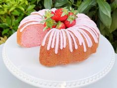 a strawberry bunt cake with icing and strawberries on top sitting on a white plate