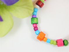 a colorful beaded necklace on a white surface next to a purple and green flower