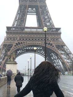 a woman is standing in front of the eiffel tower on a rainy day