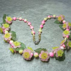 a pink and yellow flower necklace with green leaves on the bottom is laying on a gray surface