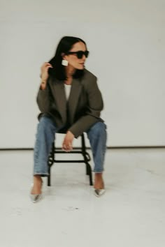 a woman sitting on top of a chair in front of a white wall wearing sunglasses