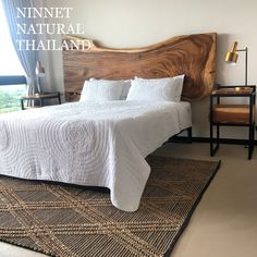 a bed with white sheets and pillows on top of a wooden headboard next to a window