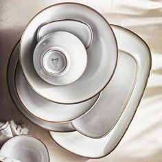 a stack of white dishes sitting on top of a bed next to a cup and saucer