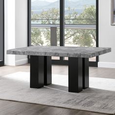 a marble table with black metal legs in front of a large window overlooking the ocean