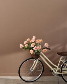 a bicycle with flowers in the basket parked next to a pink wall and wooden chair